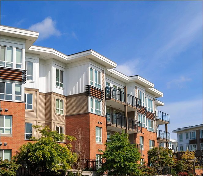 A row of apartment buildings with trees in front.